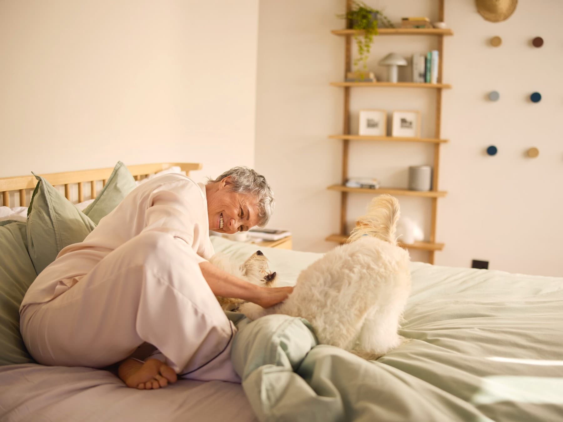 Yatakta bir köpeği okşayan gülümseyen bir kadın