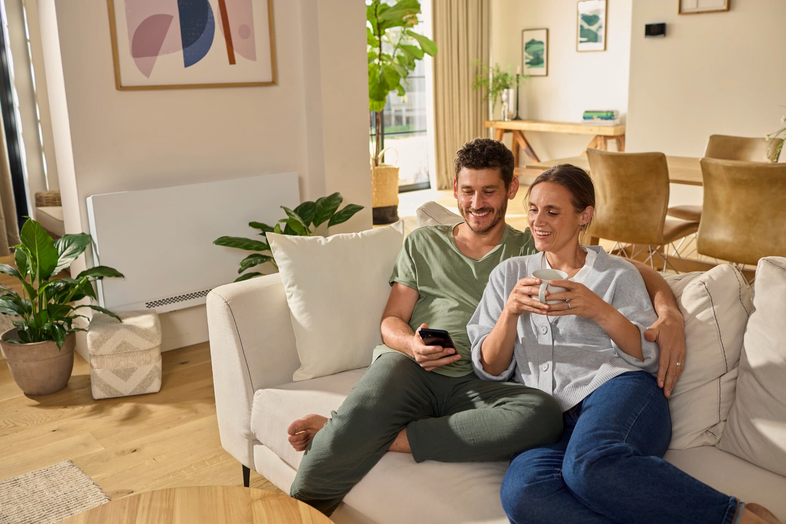 Arka planda bir aroVAIR plus fan coil ünitesi bulunan kanepede dinlenen çift