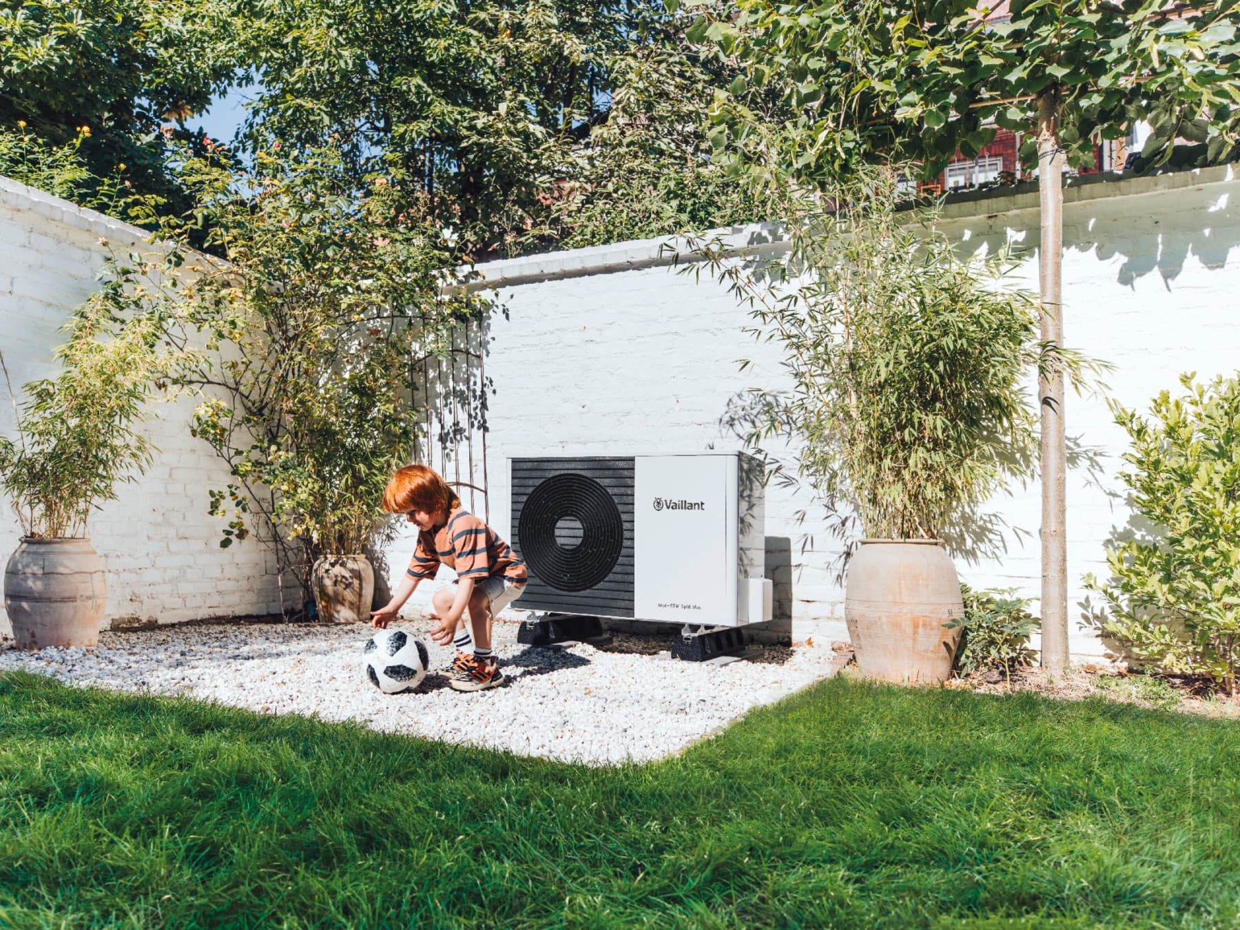 bahçede bir vaillant ısı pompasının önünde top oynayan çocuk
