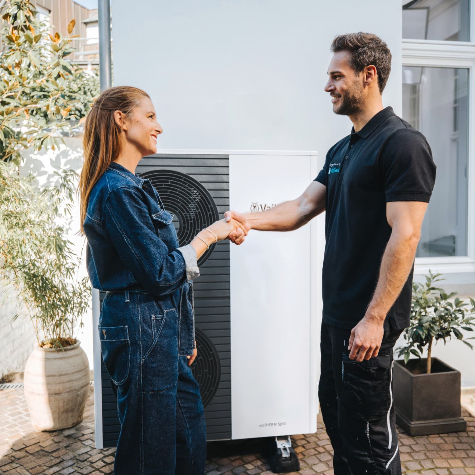 Bir ısı pompasının önünde el sıkışan bir kadın ve Vaillant servis elemanı