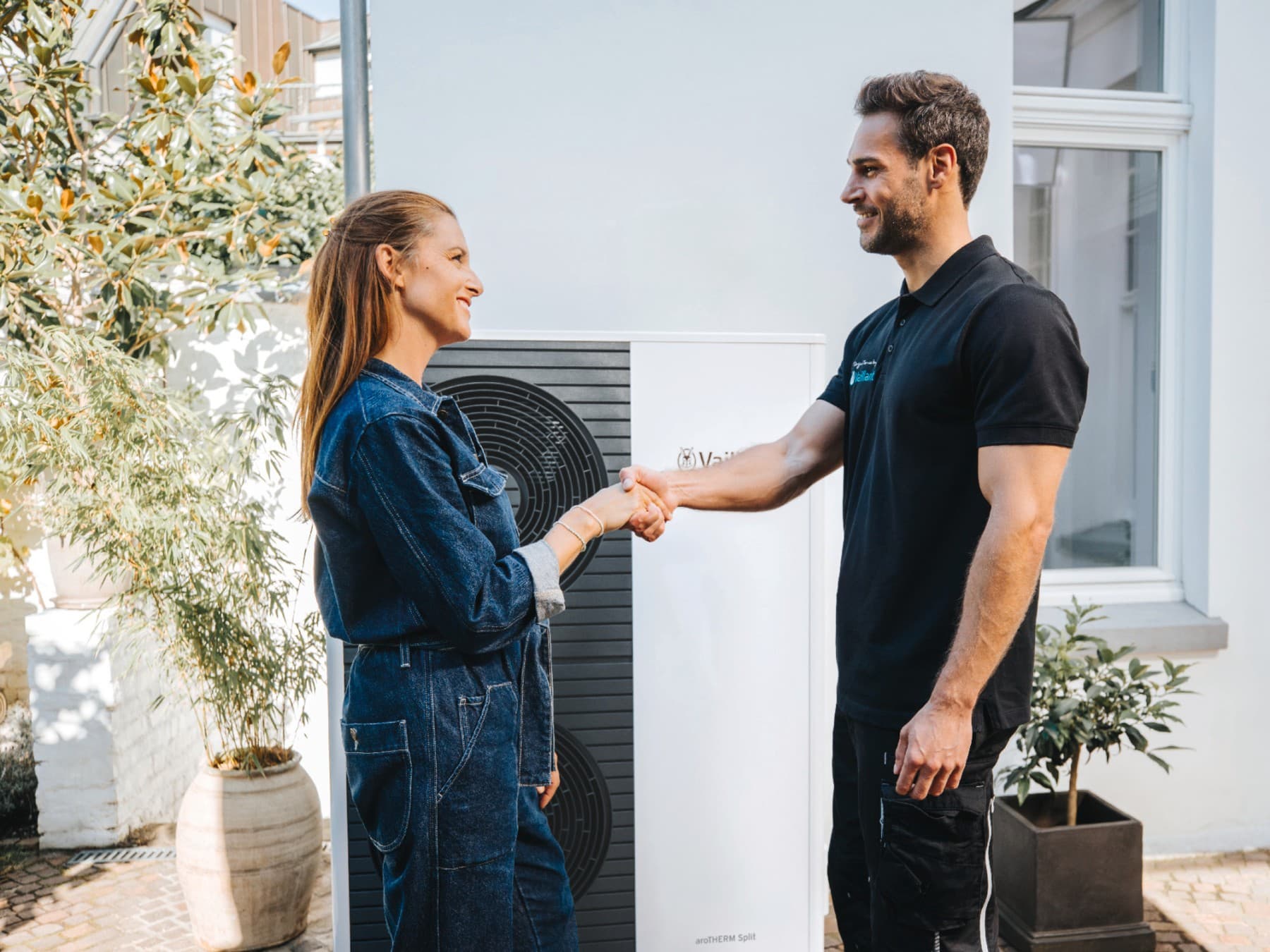 Bir ısı pompasının önünde el sıkışan bir kadın ve Vaillant servis elemanı