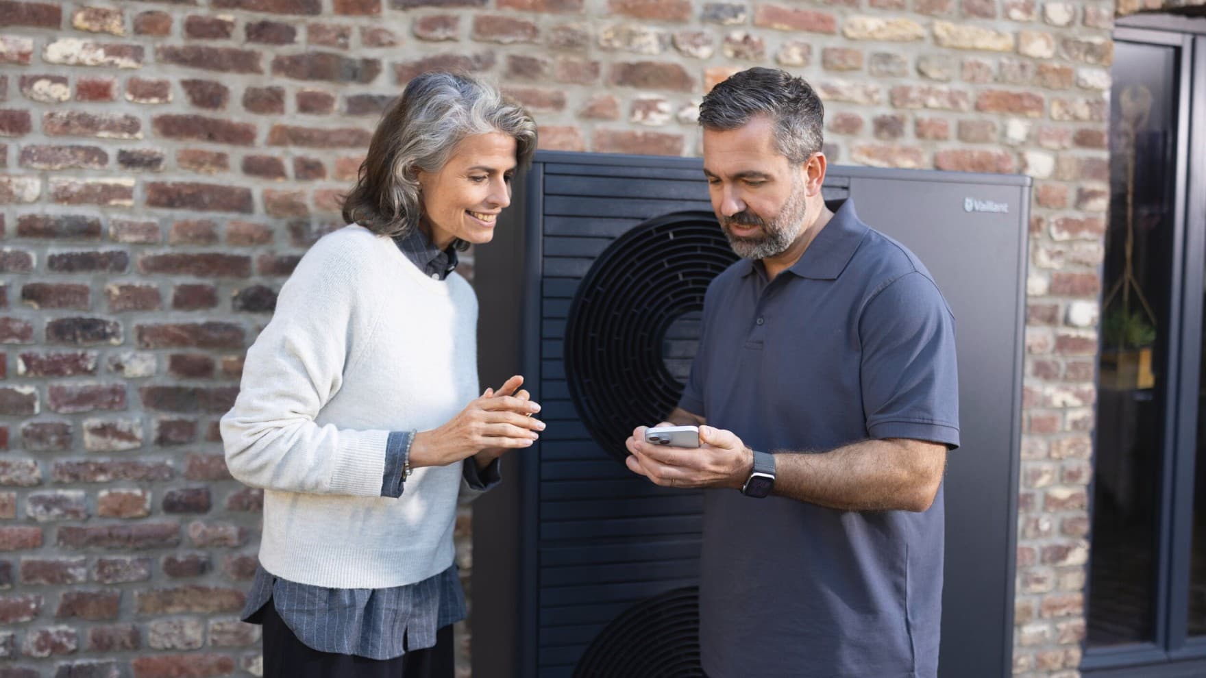 Isı pompasının önünde bir kadına myVAILLANT uygulamasını anlatan montajcı